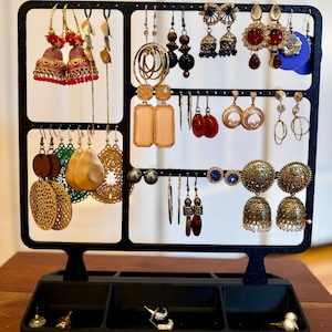 May include: A black metal earring display stand filled with various earrings. The earrings include gold, red, and blue colors, with different shapes and styles. The stand has a tray at the bottom for additional earrings.