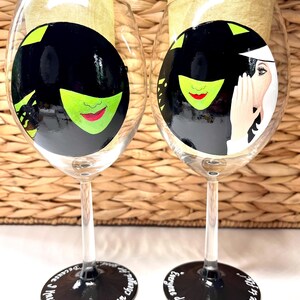 May include: Two black and white wine glasses with green and red painted designs. The glasses have black stems and bases with white text. The text on the left glass reads "I knew you, I have been changed". The text on the right glass reads "Everyone deserves the chance to fly".
