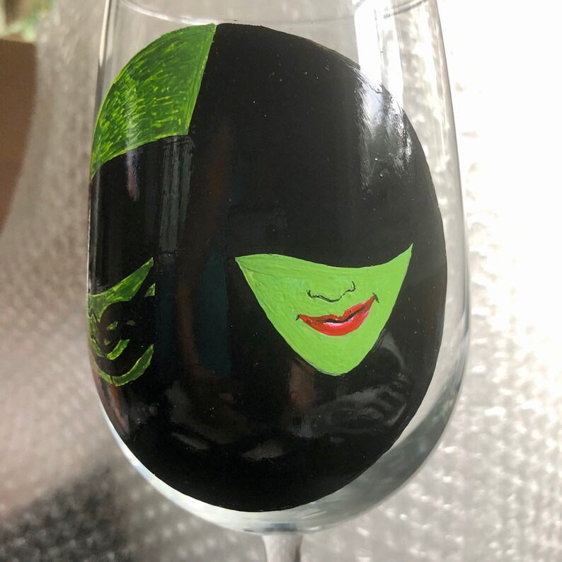 May include: A hand-painted wine glass with a black and green portrait of the Wicked Witch of the West from the Wizard of Oz.
