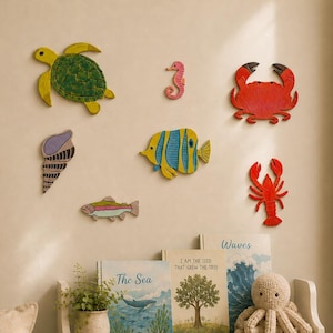 Puede incluir: Una colección de siete decoraciones de pared de madera con forma de criaturas marinas, que incluye una tortuga verde, un caballito de mar rosa, un cangrejo rojo, una concha morada, un pez amarillo y azul, un pez pequeño y una langosta roja.