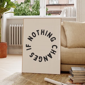 May include: A framed art print featuring the phrase "IF NOTHING CHANGES" in a circular design. The black text is set against a cream backdrop. The print is placed in a living room, propped up against a sofa.