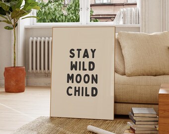 May include: A framed print with the words "STAY WILD MOON CHILD" in black block letters. The print is displayed in a room with a beige sofa, a potted plant, and a window.