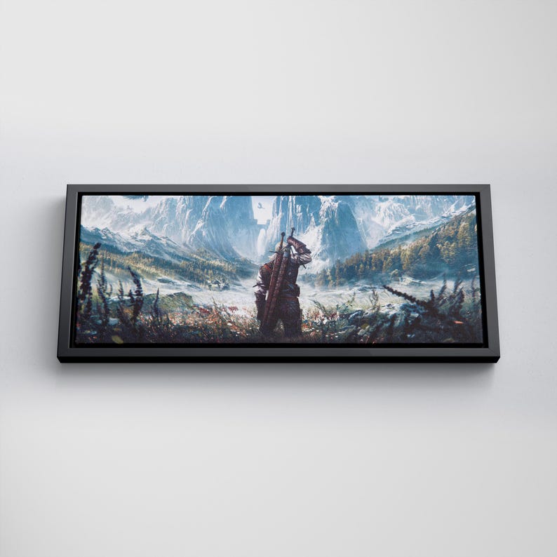 May include: A rectangular wall art print in a black frame featuring a landscape illustration of a figure standing in a field, carrying a sword on their back, facing snow-capped mountains and a forest under a bright, clear sky.