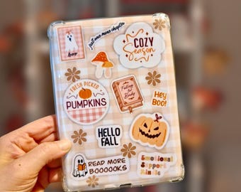 Könnte beinhalten: Eine transparente Tablethülle mit hellbeigem und weißem Vichy-Muster, verziert mit verschiedenen herbstlichen Aufklebern wie einem Geist, Kürbissen, Pilzen und Texten wie Cozy Season, Fresh Picked Pumpkins und Read More Boooooks.