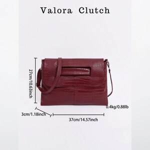 Peut inclure: Un sac Valora Clutch bordeaux avec une finition textur&eacute;e. Le sac mesure 37 cm de large, 27 cm de haut et 3 cm de profondeur. Il p&egrave;se 0,4 kg. Le sac a une bandouli&egrave;re et une forme rectangulaire.