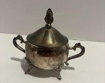 vintage silver-plated, lidded, and footed sugar bowl.Design Details: The bowl features ornate handles, a floral finial on the lid, and stand