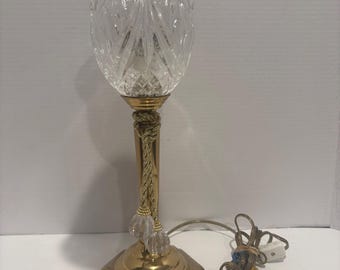 La lámpara cuenta con una pantalla de cristal estriado y una base pulida en tono dorado.