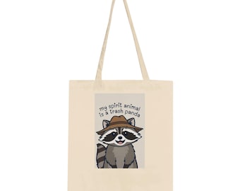 Könnte beinhalten: Cremefarbene Tragetasche mit einem Cartoon-Waschbären mit Hut. Der Waschbär hat graues und braunes Fell und einen lächelnden Ausdruck. Auf der Tasche steht "my spirit animal is a trash panda."