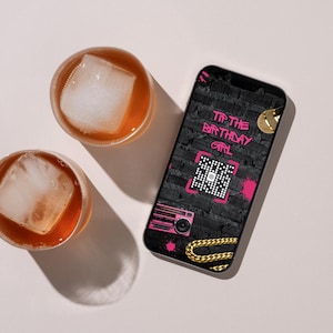 May include: Two glasses of amber-colored liquid with large ice cubes sit next to a smartphone. The phone displays the text "Tip the Birthday Girl" in pink graffiti style, along with a QR code, boombox, and gold chain design.