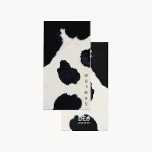 May include: Two rectangular cards featuring a black and white cow print pattern. The top card displays the word WHIMSY in a vertical gothic font. The bottom card features the text DES ARLENE CO. in a gothic font over the cow print background.