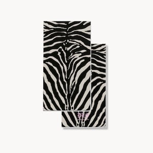 May include: Two rectangular paper napkins featuring a bold black and off-white zebra stripe pattern. The bottom napkin displays small, light pink text near the center that reads "DES" above the word "ABLINCO."