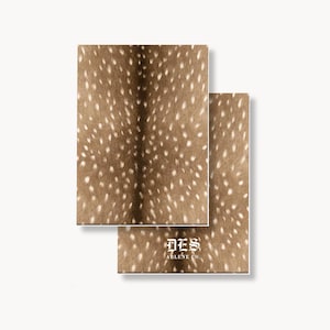 May include: Two rectangular notebooks featuring a brown and white spotted deer hide pattern. The front notebook displays the white text DES ARLENE CO. in a stylized gothic font centered near the bottom, with a smaller sans-serif font below.