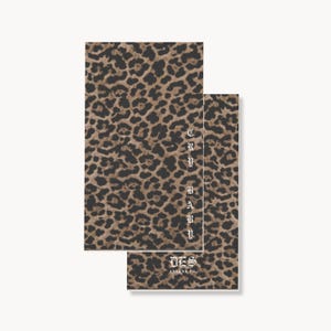 May include: Two rectangular cards featuring a brown and black leopard print pattern. The top card displays the vertical text CRY BABY in a white gothic font. The bottom card features the text DES ARLENE CO in a white gothic font at the bottom.