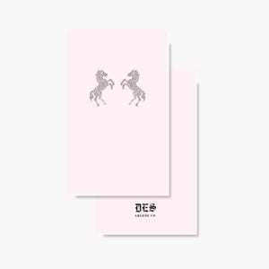 May include: Two rectangular light pink cards. The top card features two mirrored horse silhouettes composed of small dark dots. The bottom card displays the black text DES ARLENE CO. in a gothic font style centered near the bottom edge.