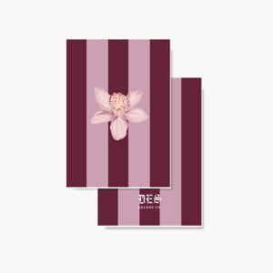 May include: Two rectangular cards featuring a vertical striped pattern in alternating shades of deep burgundy and light mauve. The front card displays a single pale pink orchid illustration in the center. The back card shows the white text DES ARLENE CO.