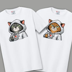 May include: Two white t-shirts featuring cartoon cats wearing hoodies and holding mugs. One cat is gray, the other is orange. Each mug has a heart and the words "I Love Mom". The shirts have the brand logo "Super Tees" at the top.