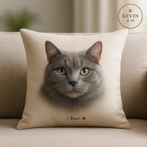 Könnte beinhalten: Ein quadratisches beiges Kissen mit einem detaillierten Porträt einer grauen Katze mit grünen Augen. Der Name der Katze, "Oliver", ist unter dem Bild mit einem Herzsymbol aufgedruckt. Das Kissen hat den Text "KEVIN & Me" in einem Kreis.