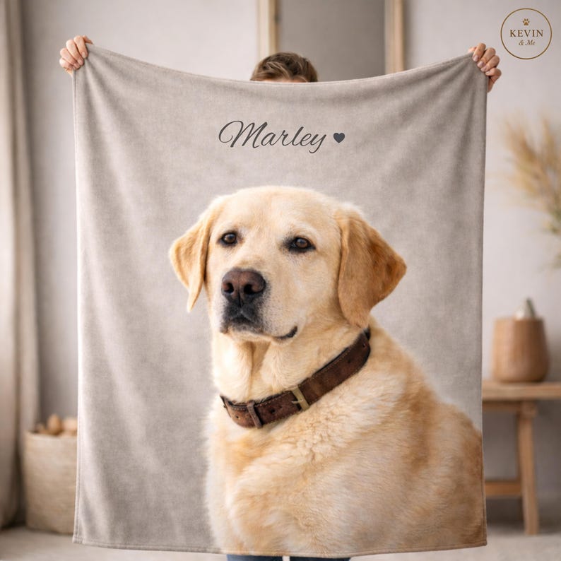 Op de afbeelding: Een beige deken met een portret van een gele Labrador Retriever met een bruine halsband. De naam "Marley" staat in script boven de hond, met een hartsymbool. De deken wordt door een persoon omhoog gehouden.