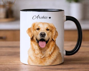 Op de afbeelding: Witte keramische mok met een zwarte handgreep en rand, met een portret van een Golden Retriever-hond. De naam van de hond, "Archie", staat boven de afbeelding gedrukt. De mok staat op een houten oppervlak.