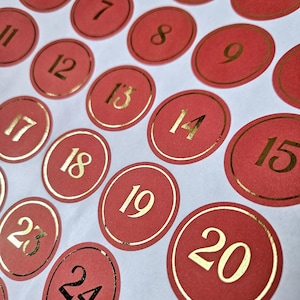 May include: A sheet of red and gold circular stickers with numbers 1 through 24. The stickers are arranged in rows and columns on a white background.