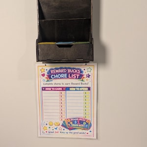 May include: A dark stained wooden chore chart organizer with multiple slots and a "Reward Bucks Chore List" attached. The list includes sections for earning and spending reward bucks, with colorful reward bucks below.