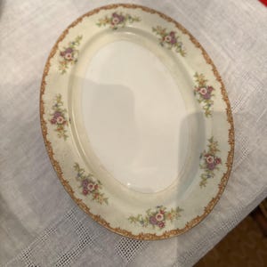 May include: Oval serving platter with a cream-colored base and a floral design. The rim features a gold-colored trim and delicate floral clusters in pink, purple, and yellow. The platter is ideal for serving appetizers or desserts.