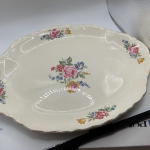 May include: An oval, off-white serving platter with a scalloped edge and gold trim. The platter is decorated with floral bouquets in pink, red, yellow, and blue. A central bouquet is surrounded by smaller floral arrangements.