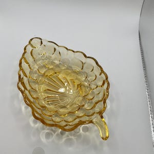 May include: A vintage amber-colored glass dish in the shape of a leaf. The dish has a textured surface with a pattern of small, rounded bumps. It features a small, pointed stem and is likely used for serving small portions.