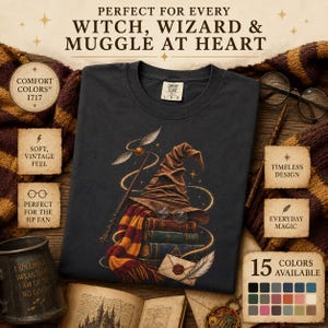 May include: A dark gray t-shirt featuring a graphic print of a brown wizard hat, a red and yellow striped scarf, a stack of books, a golden winged ball, a wand, and an envelope with a wax seal. The shirt has a Comfort Colors 1717 label.