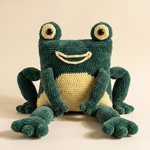 Puede incluir: Un juguete de peluche con forma de rana hecho de hilo verde oscuro y crema. La rana presenta un cuerpo de forma cuadrada, dos ojos prominentes con pupilas negras y una boca cosida de color crema. Tiene cuatro extremidades con patas palmeadas.