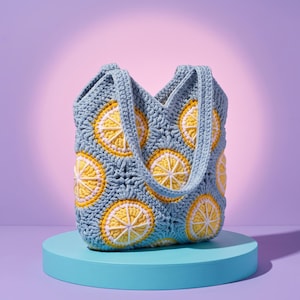 May include: A crochet tote bag constructed from light blue yarn, featuring a repeating pattern of circular lemon motifs. Each motif consists of a yellow center, a white segmented ring, and a light blue border. The bag has two integrated handles.