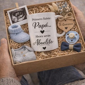 Peut inclure: Un coffret cadeau avec des articles pour bébé. Il comprend une tasse blanche avec du texte en espagnol, une chaussure de bébé, un body, une tétine, un nœud papillon et une photo d'échographie. La boîte est remplie de papier déchiqueté.