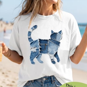 May include: White t-shirt featuring a printed design of a cat made of denim patches. The cat design is in shades of blue and has a faux patchwork effect. The text on the image says, "This is a printed design with a faux patchwork effect, not actual patchwork!"