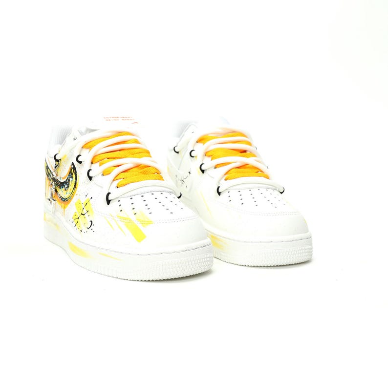 May include: White sneakers with yellow and black accents. The shoes feature yellow laces and a painted design on the side. The design includes a yellow swoosh and other artistic elements. The sneakers have a classic, low-top design.