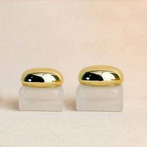 以下が含まれることがあります： 丸みを帯びた金色の蓋が付いた、2つのすりガラスの瓶。瓶は四角い形で、明るい色の表面に置かれています。蓋は光を反射し、光沢のある外観を作り出しています。