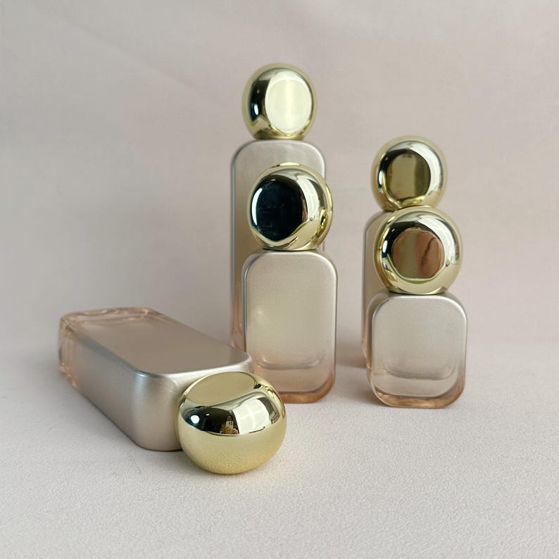 May include: A collection of perfume bottles with gold-colored spherical caps. The bottles are rectangular with rounded corners and a gradient color scheme. One bottle is lying on its side, with its cap detached.
