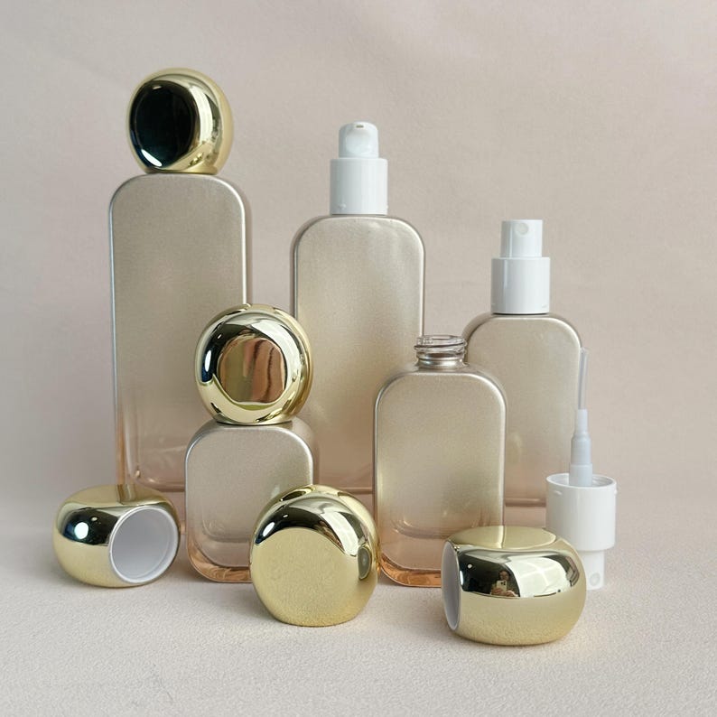 May include: An assortment of clear glass bottles and containers with gold-colored caps and white pumps. The bottles vary in shape and size, including rectangular and rounded designs. Some bottles are empty, while others have pumps or sprayers.