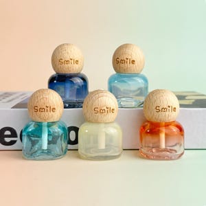 Peut inclure: Cinq petits flacons en verre avec des bases carrées arrondies et des bouchons sphériques en bois. Chaque bouchon est gravé du mot "smile" et d'un petit cœur. Les flacons sont colorés en bleu foncé, bleu clair, transparent, jaune et orange.