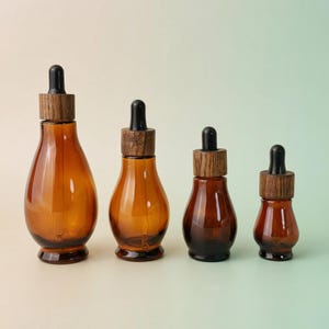 May include: Four amber glass dropper bottles of varying sizes. Each bottle has a wooden cap with a black dropper. The bottles are arranged in a row, showcasing their different heights and capacities. The background is a soft gradient.