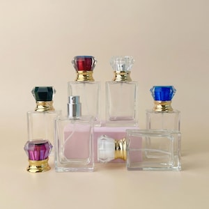 May include: An assortment of clear glass perfume bottles with colorful, gem-like stoppers. The stoppers are in various colors, including red, blue, green, and purple, with gold-colored accents. The bottles are rectangular and empty.