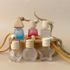 Può includere: Una collezione di profumatori per auto decorativi in varie forme e colori. I flaconi hanno coperchi in legno e sono sospesi da un cordino dorato. Le forme includono un triangolo, un quadrato, un cerchio e una stella. I flaconi sono riempiti con liquidi colorati.