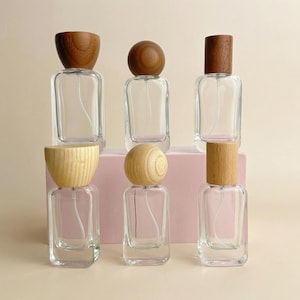 May include: Six clear glass perfume bottles with wooden caps. The caps are various shapes, including a dome, a sphere, and a cylinder. The bottles are rectangular and have a spray nozzle.