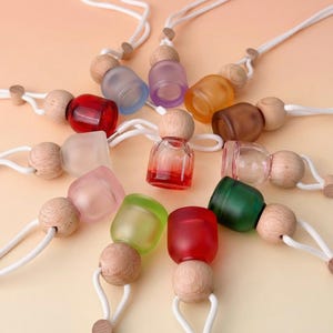 Può includere: Una collezione di piccole bottiglie di vetro colorate con tappi di legno e cordoncini bianchi. Le bottiglie sono in vari colori, tra cui rosso, verde e viola. Le bottiglie sono probabilmente per aromaterapia o oli essenziali.