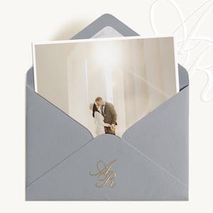 May include: A light blue envelope with a photograph of a couple kissing inside. The envelope has a gold foil monogram of the letters "A" and "R". The photograph shows a couple in a bright, airy space.