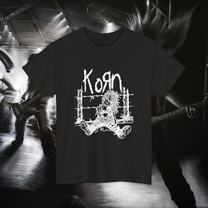 Puede incluir: Camiseta negra con el logo blanco de la banda Korn y un gráfico desgastado de una figura tras alambre de púas. El diseño es una declaración monocromática audaz, para los fans de la banda.