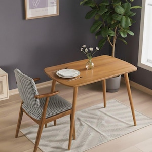 Puede incluir: Una mesa de comedor de madera marrón claro con esquinas redondeadas y cuatro patas anguladas. Una silla a juego con un estampado de pata de gallo en el asiento y el respaldo está al lado de la mesa. Un pequeño jarrón con flores está sobre la mesa.