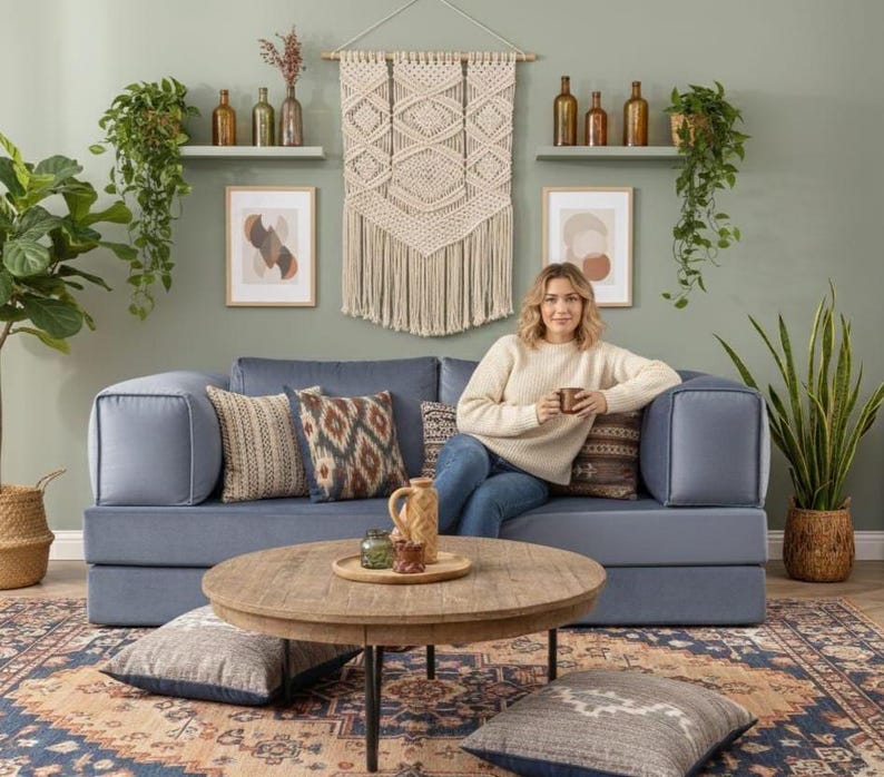 Puede incluir: Un sal&oacute;n acogedor con un sof&aacute; azul, cojines decorativos, una mesa de centro redonda de madera y una alfombra estampada. La habitaci&oacute;n est&aacute; decorada con plantas, obras de arte y un tapiz de macram&eacute;, creando un ambiente c&aacute;lido.