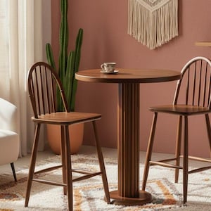 Op de afbeelding: Een houten bistrostel met twee stoelen en een ronde tafel. De stoelen hebben een spijlenrugontwerp en de tafel heeft een gefluteerde voet. De set is gemaakt van warmbruin hout en staat op een patroonkleed.