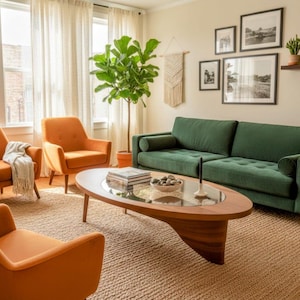 Op de afbeelding: Een woonkamer met een groene bank, twee oranje fauteuils en een houten salontafel met een glazen blad. Een grote plant in pot en ingelijste kunstwerken sieren de ruimte. De kamer heeft een neutraal kleurenpalet.