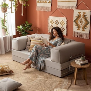 Puede incluir: Un sal&oacute;n acogedor con un sof&aacute; gris claro, cojines decorativos y una alfombra redonda de yute. La habitaci&oacute;n est&aacute; decorada con tapices de pared tejidos y plantas colgantes, creando un ambiente c&aacute;lido y acogedor.